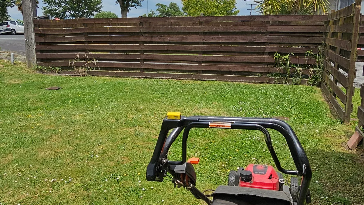 Mower on a lawn by a wooden fence
