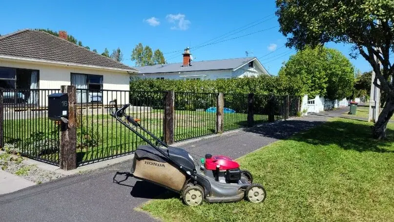 Honda mower on a freshly cut front lawn with the neighbours' houses over the fence, the customers who see you turn up every second week