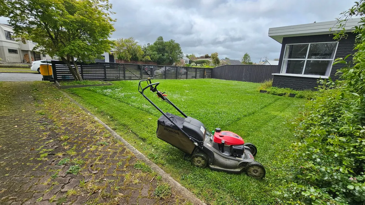 A Honda mower on a freshly striped front lawn beside a paved path and a dark modern house