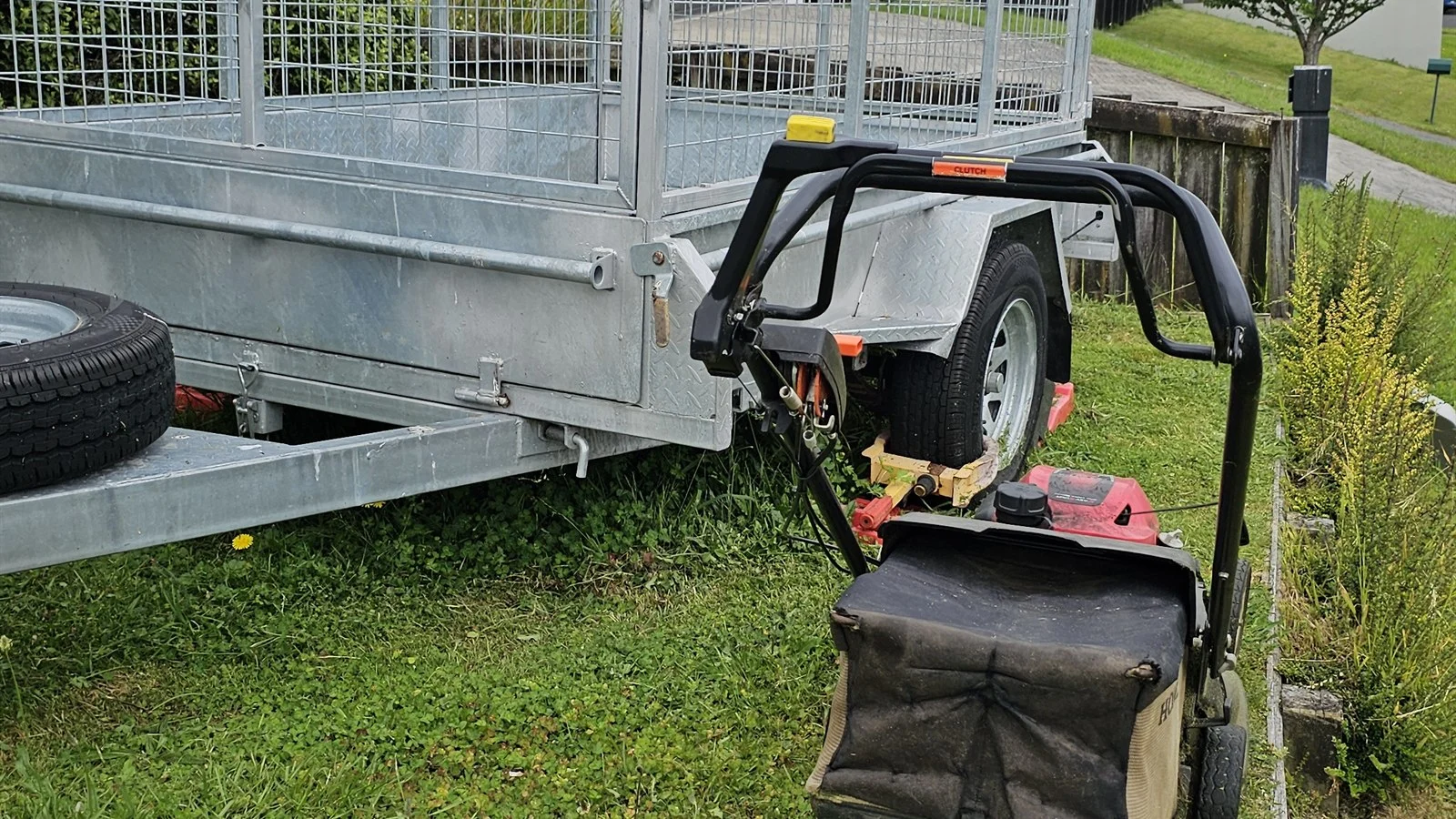 Push mower with catcher loaded beside a caged trailer, clippings taken away after a lawn mowing job