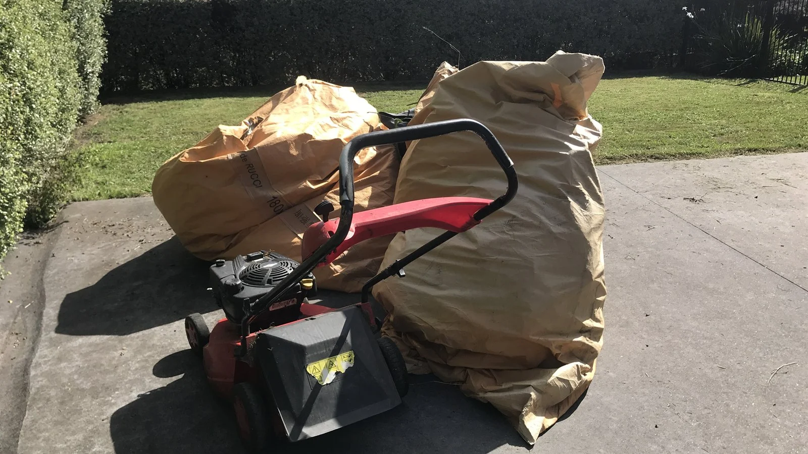 Two full paper sacks of grass clippings beside the mower on a customer's driveway, ready to go on the van