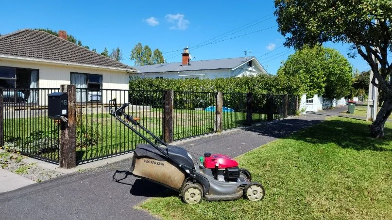 Honda mower on a freshly cut front lawn with the neighbours' houses over the fence, the customers who see you turn up every second week