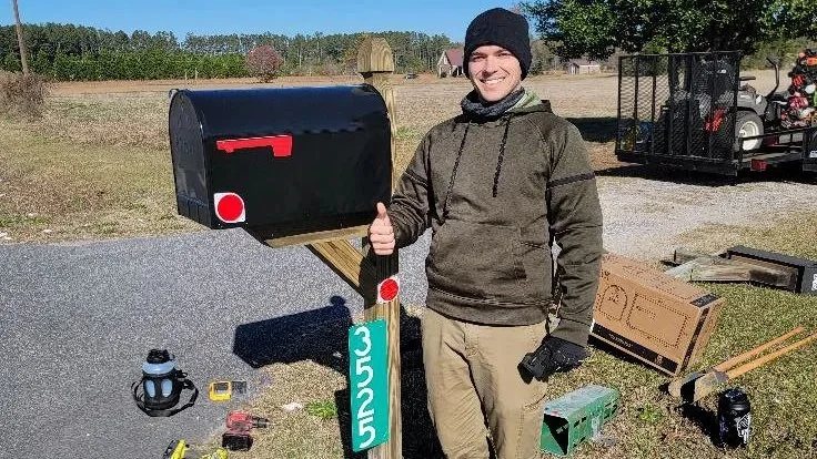 Lawn care operator standing beside a customer's mailbox on a rural job, the moment to send the quote text when nobody was home