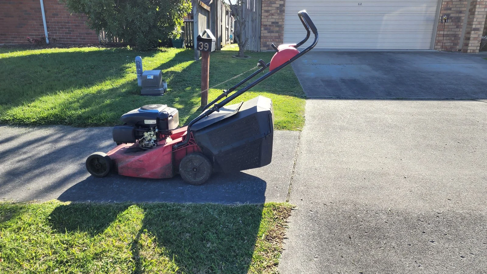 Push mower on a driveway in low winter sun, a lawn care round still running through the off season