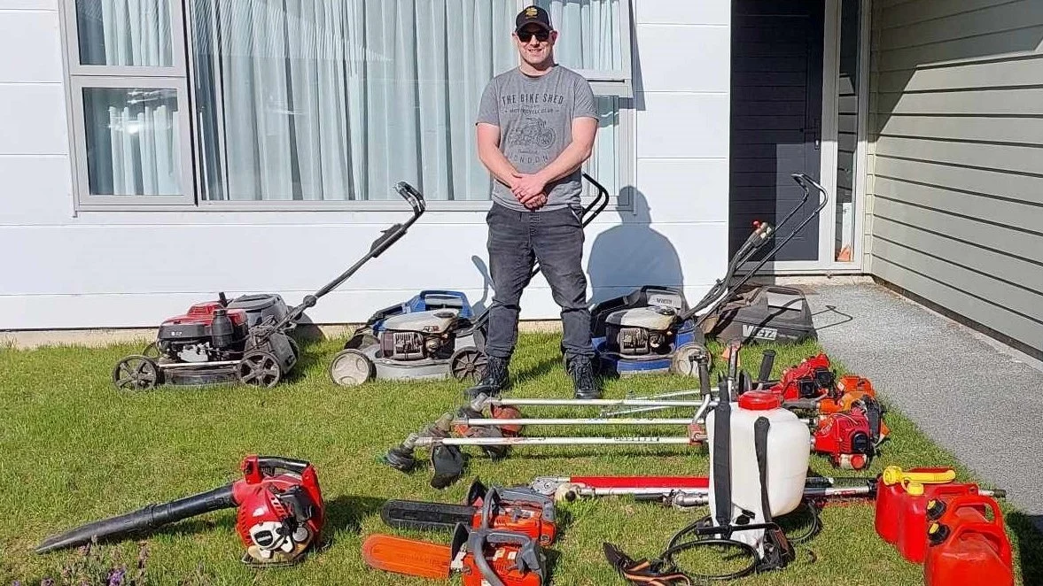 Full-time lawn care operator standing with three mowers, trimmers, blower, chainsaws and sprayer laid out on a lawn