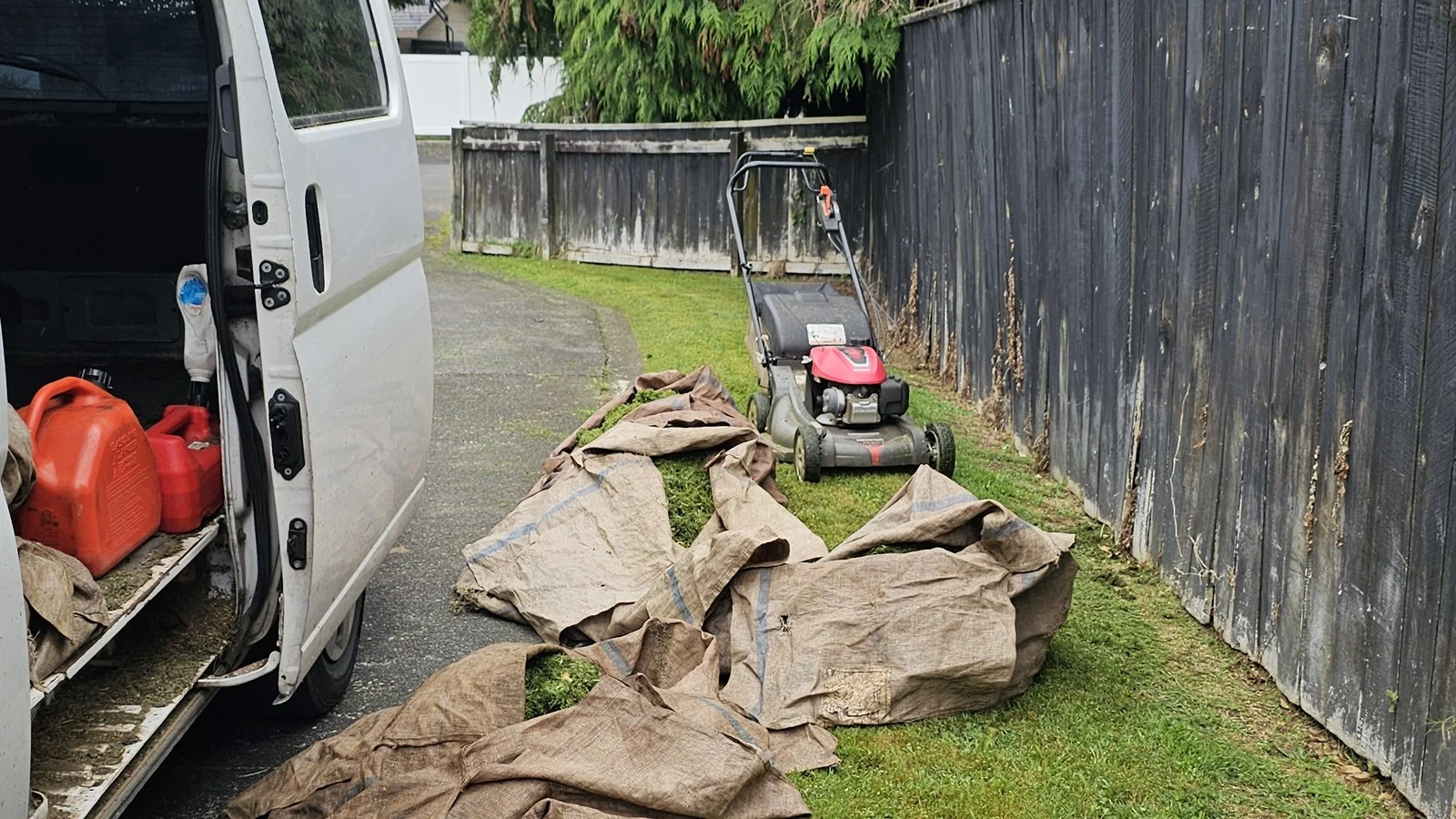 No trailer needed for a lawn mowing side hustle: push mower, fuel cans and clipping sacks laid out beside an open van